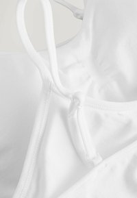 Vit sport-bh med justerbara remmar, i mjukt bomullsmaterial, och en krok-och-lopp-stängning på baksidan.