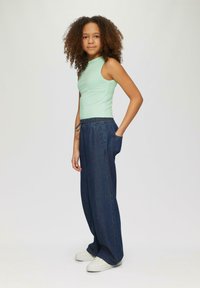 Hellgrünes, geripptes, ärmelloses Oberteil, kombiniert mit dunkelblauen, weit geschnittenen Jeans mit elastischem Bund und Taschen, getragen mit weißen Sneakers.