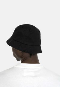 Cappello a secchiello in cotone nero con una texture soffice e una larga tesa, caratterizzato da una corona arrotondata e dettagli di cucitura sottili.