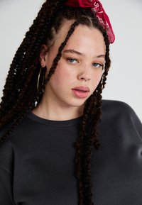 Mørk grå hettegenser med rund halslinning og en glatt tekstur. Modellen har langt, teksturert hår med et rødt hodebånd og hoopsølv.