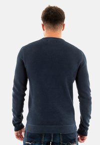Maglione a maglia testurizzata di colore blu navy con scollo rotondo, maniche lunghe e polsini e orlo a coste, visto da dietro.