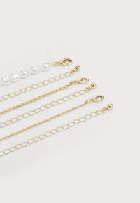 Cadenas en tono dorado con eslabones de diferentes tamaños y una sección de perlas blancas. Cada una tiene un cierre de langosta para su sujeción.