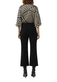 Zwarte brede broek gecombineerd met een beige en zwarte gestreepte blouse met lange mouwen en een keyhole-detail aan de achterkant.