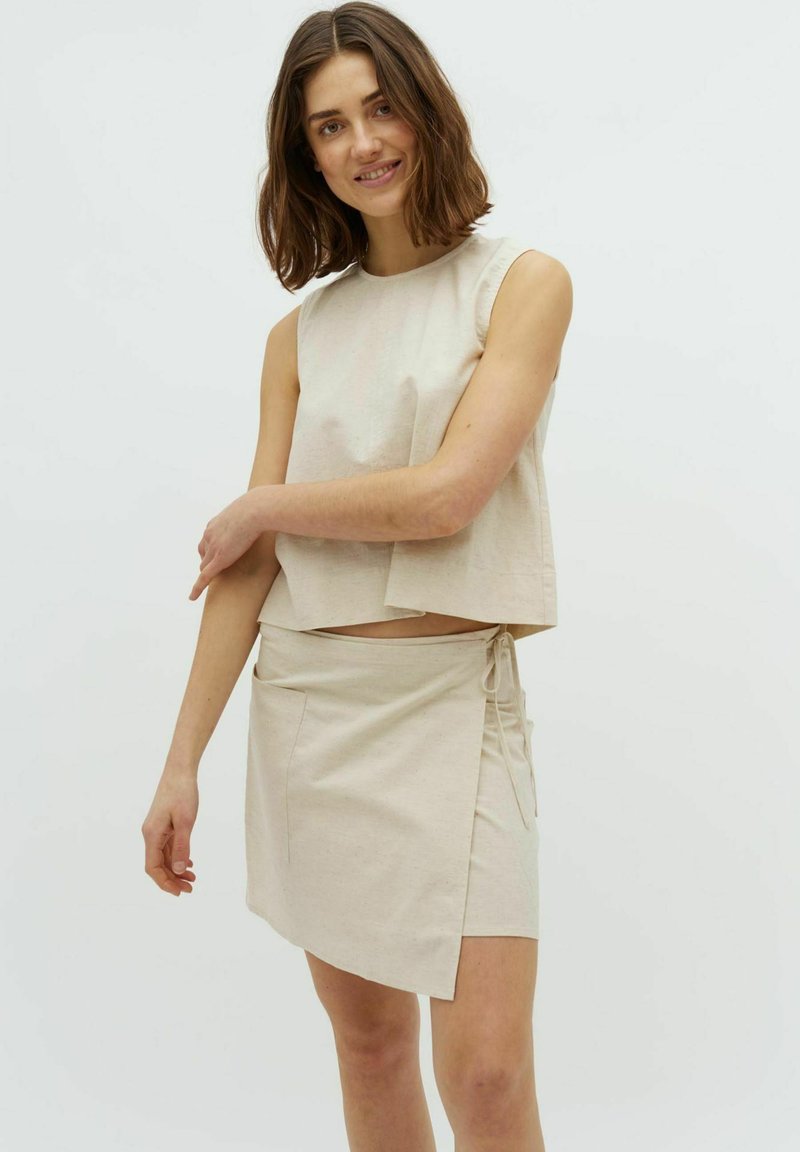 Helles beige Zweiteiler-Outfit mit einem Cropped-Top mit rundem Ausschnitt und einem Wickelrock mit seitlichem Bindedetail und glatter Textur.