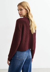 Burgundy cropped tröja med texturerad yta, featuring långa ärmar. Matchas med högmidjade blå denimjeans.