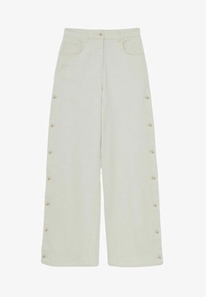 Pantalons large en coton beige clair, présentant des boutons latéraux, une poche avant et une coupe droite. Texture lisse avec une taille haute.
