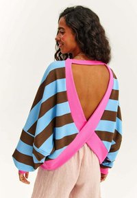 Svetr s dlouhým rukávem s modro-hnědými pruhy a růžovým akcentem, otevřeným designem zad a volným střihem. Látka vypadá měkce a strukturovaně.