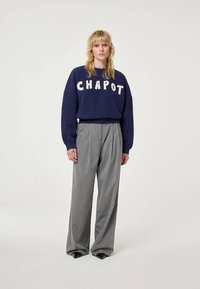 Mörkblå sweatshirt med texten "CHAPOT" i beige, kombinerad med grå randiga plisserade byxor. Båda plaggen har avslappnad passform och mjuka material.