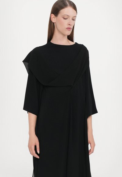Black dress with a draped neckline, wide sleeves, and flowing silhouette. Made of smooth fabric with a minimalist design and no visible patterns.