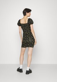 Vestido preto curto com mangas bufantes, apresentando um padrão floral amarelo. O design inclui um decote quadrado e uma silhueta ajustada.