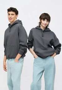 Két modell visel túlságosan nagy szürke kapucnis pulóvereket kenguruzsebbel, világoskék farmernadrággal párosítva. A kapucnis pulóvereken húzózsinórok és mandzsettás ujjú végek találhatók.