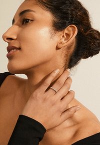 Hopeasormus, jossa on pyöreitä jalokiviä, käytetään kädessä. Mallilla on kiharat hiukset, hänellä on musta toppi, ja hänen ihonsa on sileä ja ilmeensä pehmeä.