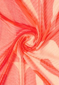 Tissu transparent rouge et pêche clair torsadé en spirale, montrant une texture tissée fine et des plis doux et fluides.