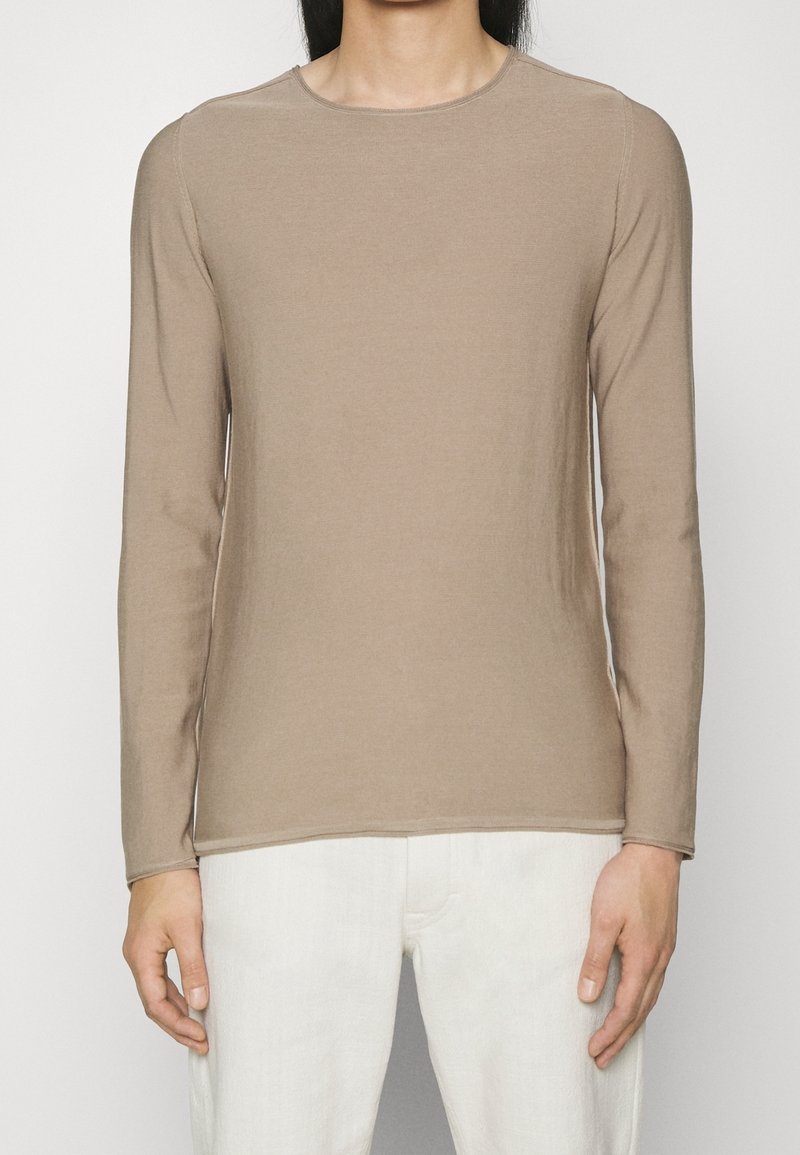 T-shirt en coton marron clair à manches longues avec un col rond et une texture lisse, associé à un pantalon écru.