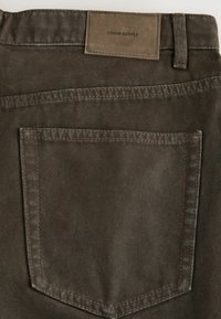 Hnědé l�átkové kalhoty s zadní kapsou, viditelným šitím a obdélníkovou koženou nášivkou s nápisem "DENIM SUPPLY."