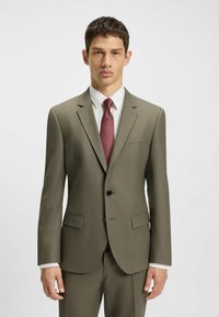 Olivgrüner Anzug mit taillierter Passform, einem Knopf, Reverskragen, zwei vorderen Taschen und einer strukturierten burgunderroten Krawatte über einem weißen Hemd.