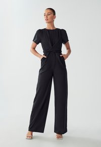 Zwarte jumpsuit met korte pofmouwen, wikkelfront ontwerp, brede pijp-silhouet en zijzakken, gemaakt van een gladde stof.