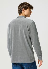 Koszulka polo z długim rękawem w szarym materiale o teksturowanym wykończeniu, z klasycznym kołnierzykiem i bocznymi rozcięciami dla większej swobody ruchów.