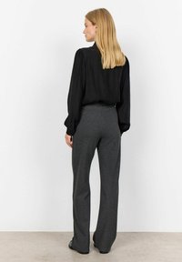 Must have struktuurse mustriga musta toppi, millel on puhv sleeves, koos hallide triibuliste pükste kätte. Püksid on vööst hästi istuvad ja allääres laienevad.