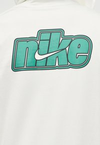 Λευκό ύφασμα με μεγάλο κομψό λογότυπο "nike" σε τιρκουάζ και μαύρο περίγραμμα, που περιλαμβάνει το λευκό σήμα Nike swoosh ενσωματωμένο μέσα στα γράμματα.