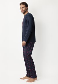 Top de manga larga azul marino con un diseño gráfico, combinado con pantalones de estampado que presentan motivos rojos sobre un fondo azul marino. Tela suave, corte holgado.