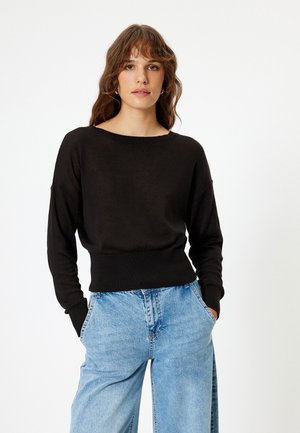 Black knit sweater with wide neckline, long sleeves, and ribbed hem. Paired with light blue wide-leg jeans. Smooth texture, classic fit.