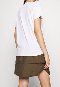 Vit bomulls t-shirt med korta ärmar, uppvisad tillsammans med en khaki kviltad kjol med ett lagerdesign och diamantmönster.