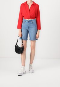 Czerwona krótka bluzka z długimi rękawami, jasnoniebieskie szorty dżinsowe z wysokim stanem, czarna torebka z ćwiekami i białe trampki typu high-top.