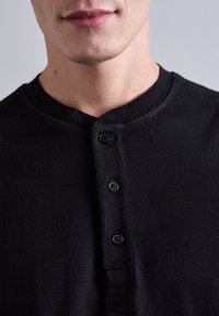 Čierna henley polo tričko vyrobené z bavlny, s guľatým výstrihom, tromi gombíkmi vpredu a textúrovanou tkaninou.