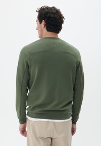 Zeleno sweatshirt s sproščenim krojem, rebrastimi manšetami in robom, gladko teksturo in šivom čez hrbet.