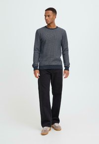 Marineblauer Strickpullover mit strukturiertem Muster, Rundhalsausschnitt und gerippten Bündchen, kombiniert mit schwarzen weit geschnittenen Hosen und grauen Sneakers.