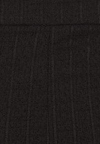 Tissu en tricot noir présentant un motif texturé avec des côtes verticales et de subtiles variations d'épaisseur. Texture douce et légèrement duveteuse.