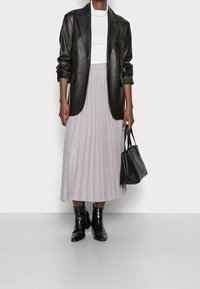 Zwarte leren blazer, witte aansluitende t-shirt, lichte geplooide rok, zwarte enkellaarsjes en een kleine zwarte handtas. Soepele texturen en zachte kleuren.