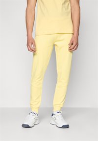 T-shirt en coton jaune associé à un jogging jaune assorti, avec une coupe ajustée et des poignets côtelés. Des baskets blanches complètent le look.