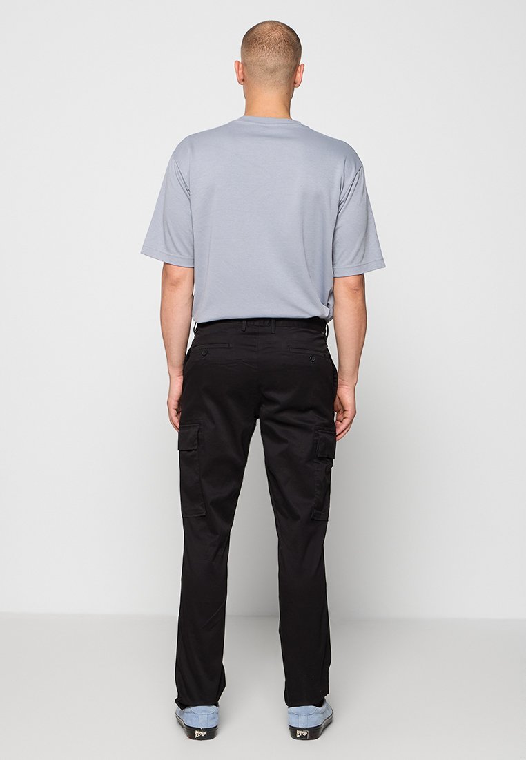 T-shirt gris à manches courtes associé à un pantalon cargo noir avec des poches latérales et une coupe droite. Des chaussures bleues complètent la tenue.