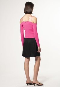 Top a maglia rosa aderente con spalle scoperte e maniche lunghe, abbinato a una gonna nera a trapezio e sandali neri col tacco. Tessuto strutturato e spalline visibili.