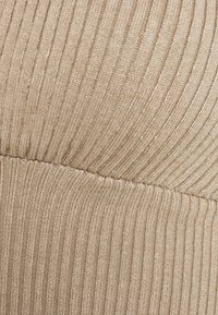 Beżowa tkanina prążkowana o miękkiej fakturze, z wyraźnymi pionowymi paskami i detalem szwu w poziomej części środkowej.