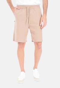 Pantaloni corti beige realizzati in tessuto leggero, con vita regolabile, tasche laterali e un taglio comodo, abbinati a sneaker bianche.