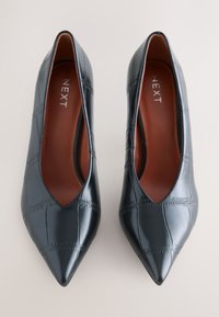 Paire de chaussures noires pour femmes à bout pointu avec motif cousu et doublure intérieure marron, vues de dessus sur un fond clair.