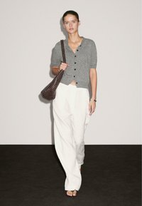 Cardigan grigio a maglia con bottoni e maniche corte, indossato sopra un pantalone bianco dalla vestibilità ampia, abbinato a una borsa a tracolla scura. Design minimalista.