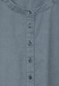 Camicia azzurra chiaro con colletto rotondo e sei bottoni frontali, caratterizzata da un tessuto con una trama testurizzata.
