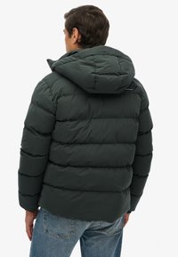 Ciemnozielona kurtka puchowa z kapturem. Pikowana konstrukcja i wytrzymały materiał. Posiada subtelne logo na plecach oraz elastyczne mankiety.