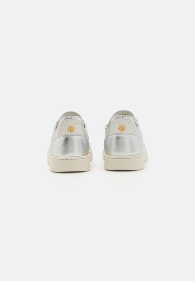 Silver metallic sneakers with a smooth finish, beige rubber soles, and a small yellow logo accent on the back. Rounded heel design.