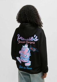 Felpa nera con grafiche colorate sul retro. Il design include un personaggio che tiene un hamburger, con il testo "Paddle's Smash Burgers" e "Best in Town."