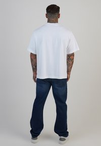 Camiseta de algodón blanca de manga corta, combinada con unos vaqueros de denim azul de corte holgado. Diseño liso sin patrones ni acentos visibles.
