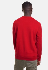 Sudadera roja de cuello redondo con mangas largas, puños y dobladillo acanalados, hecha de una tela suave. Vista trasera que muestra una textura lisa sin gráficos.