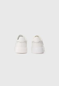 Pair of white low-top sneakers shown from the back on a plain light grey background.