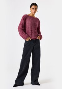Donkerroze kabelgebreide trui met een brede halslijn en lange, losse mouwen; gecombineerd met hooggewaadde, wijde zwarte jeans met subtiele textuur.