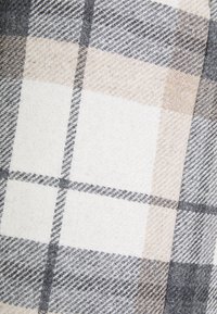 Tissu en plaid en laine présentant un mélange de carrés beige clair, gris et blancs, avec une surface douce et texturée et de fines lignes contrastées.