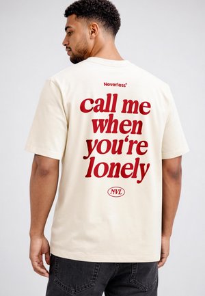 Man wearing a cream t-shirt with red text on the back that reads "call me when you're lonely" and "Neverless" near the neckline.